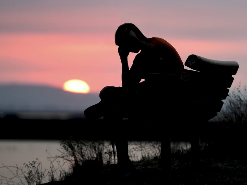 person on bench at waterfront at sunset