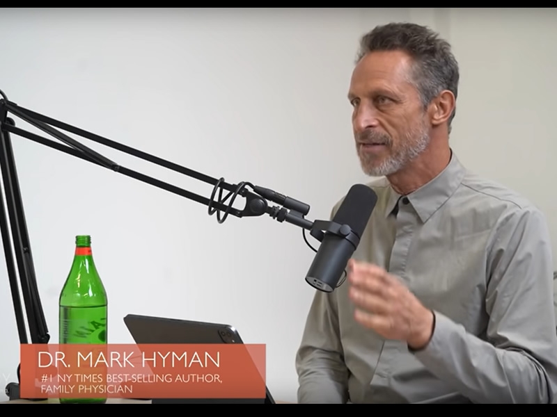 Mark Hyman seated at a table with a computer and large microphone