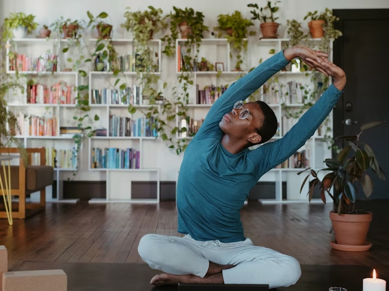 Person seated on floor and stretching with arms overhead.