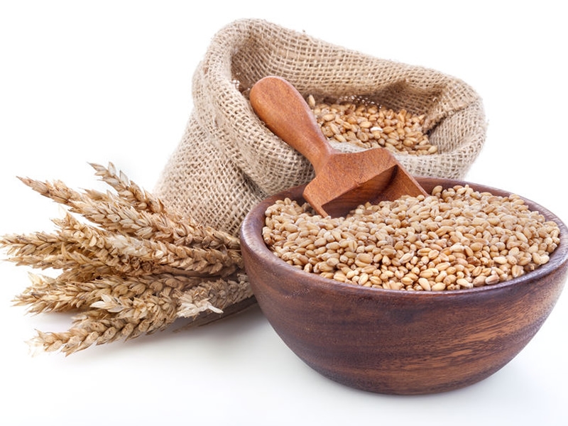 stalks of wheat next to wheat germ in a wood bowl and burlap bag