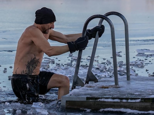 Man stepping down ladder at end of dock into water with floating chunks of ice.
