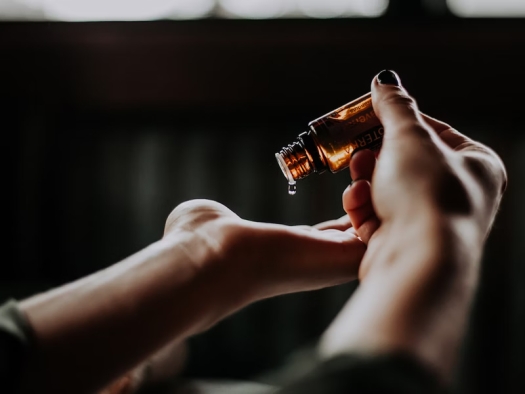 Person holding a small amber glass bottle and dropping a drop of liquid into their hand.