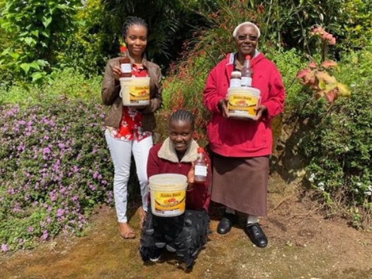 Three African women holding buckets filled with food and supplies.