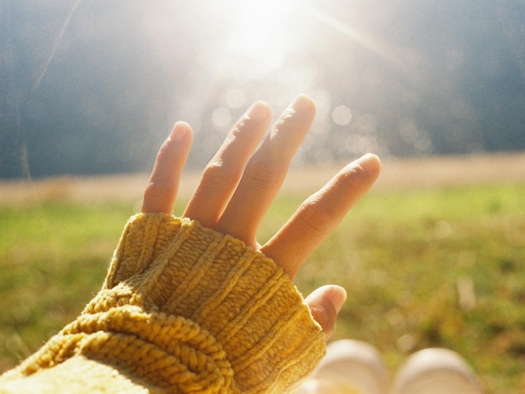 Person's hand reaching up toward morning sun.