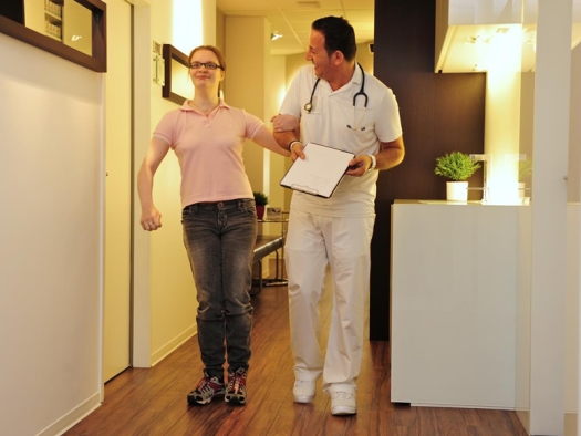 Woman walking down hall holding arm of medical personnel.