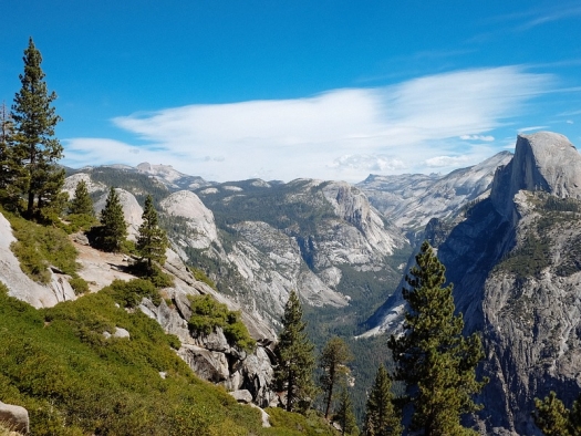 gray rocky mountains with green bushes and pines in foreground and blue sky