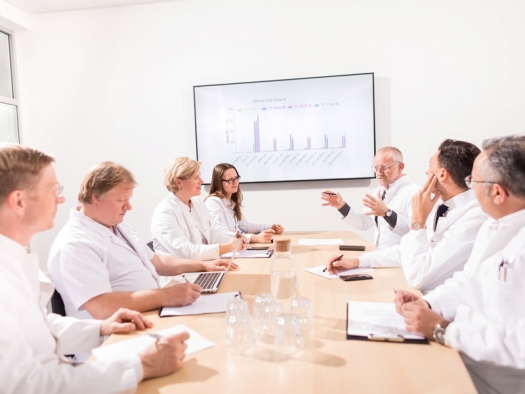 doctors meeting around a conference table with a chart projected on the screen