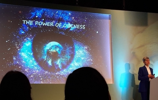 Lynne McTaggart on stage presenting; slide behind her says "The Power of Oneness" with a starfield