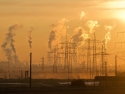 smokestacks and electrical wires with smoke rising at sunrise creating a smoky orange sky