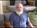 Andrew Weil seated on a couch, with his dog next to him, talking to the camera.