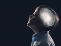 Child looking up with eyes closed; white light in shape of brain is superimposed on child's head to illustrate brain activity.