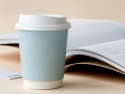 paper coffee cup with lid next to an open book