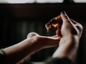 Person holding a small  amber glass bottle and dropping a drop of liquid into their hand.