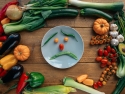 green chili pepper and orange tomatoes on white ceramic plate form a "sad face" surrounded by other fruits and vegetables