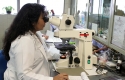woman in white coat looking through microscope in a lab