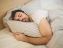 young man with short beard sleeping on bed with gray and white striped sheets and pillow