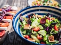 Large bowl of salad with platter to side with tomatoes and onions.