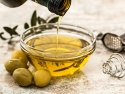 Olive oil being poured into a glass bowl with olives on the counter next to the bowl