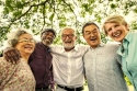 Five seniors, men and women, shoulder to shoulder, laughing together in a park