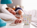 sleepy woman in bed hitting snooze button on phone next to coffee cup