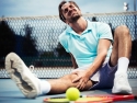 man sitting on tennis course holding his knee and grimacing in pain