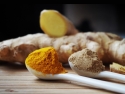 powered turmeric and ginger in white spoons with raw ginger in background 