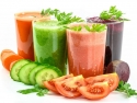 four glasses of veggie juice with cut carrots, cucumbers, tomatoes, and beets