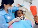 Woman in dental chair, looking in mirror as dental hygienist works