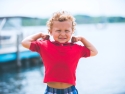 young boy near waterfront with arms raised showing how strong he is