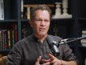 Zach Bush desk with microphone with bookcase in background.